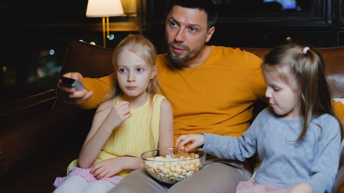 Akşam lambası altında kanepede film izleyen bir baba ve iki kızı